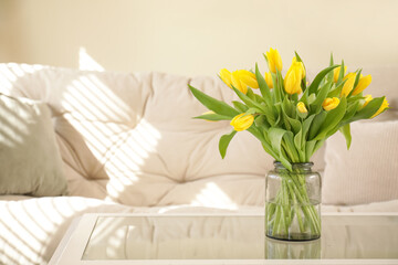 Vase with tulips on glass coffee table in living room