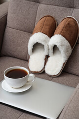 Composition with slippers, cup of coffee and modern laptop on sofa