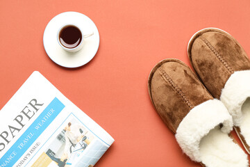 Pair of soft brown slippers with cup of tea and newspaper on red background. Top view