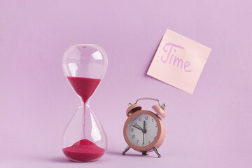 Sticky note with word TIME, hourglass and alarm clock on lilac background. Time management concept