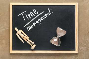 Blackboard with text TIME MANAGEMENT, wooden human figure and hourglass on beige background. Top...
