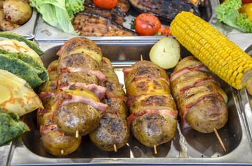 Delicious grilled skewered potatoes wrapped with bacon slices, served alongside corn on the cob and...