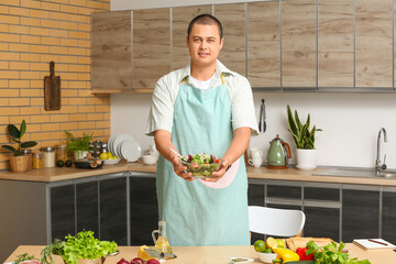 Young man with prepared vegetable salad in kitchen