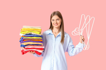 Young woman with stack of colorful clothes and hangers on pink background