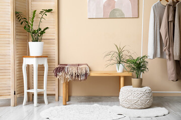 Bench, folding screen and houseplants near beige wall in room