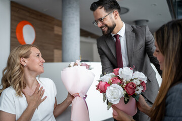 Managers giving flowers to grateful female coworker in office lobby