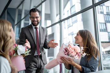 Manager congratulating female employees giving flowers bouquet in office