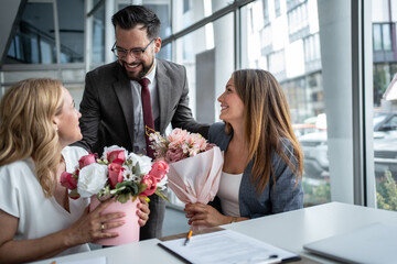 Businessman giving flowers to female colleagues in office