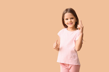 Portrait of happy little girl pointing at something on beige background