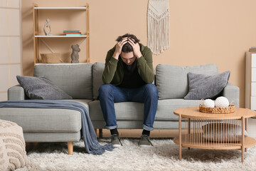 Depressed young man sitting on sofa at home