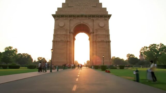 Majestic India Gate monument with people strolling along a path towards the archway at sunset.