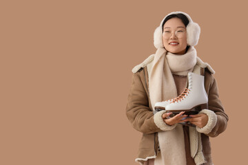 Beautiful young happy Asian woman with ice skates on beige background