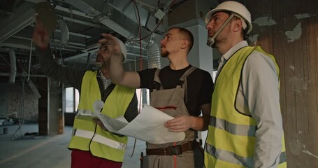 Construction engineers and a worker review blueprints and discuss progress inside a building under construction. - Powered by Adobe