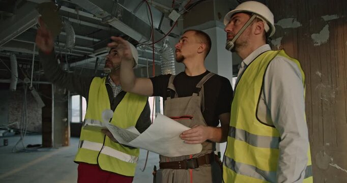 Construction engineers and a worker review blueprints and discuss progress inside a building under construction.
