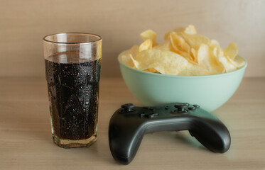 A relaxed scene featuring a stack of potato chips (similar to Pringles), a video game controller, and a glass of soda. This setup captures the essence of casual leisure time, perfect for gaming sessio