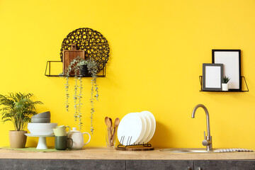 Counters with sink and utensils near yellow wall in kitchen