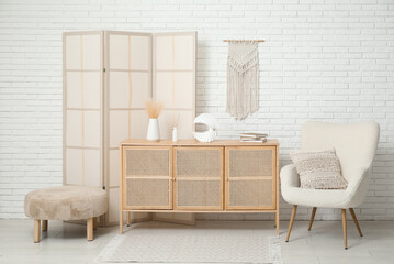 Interior of modern room with folding screen, pouf, armchair and chest of drawers