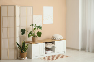 Interior of modern room with folding screen, houseplants and bench near beige wall