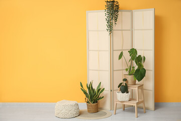 Interior of room with folding screen and houseplants near yellow wall
