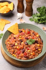 Tasty chili con carne in bowl and nachos on grey table, closeup