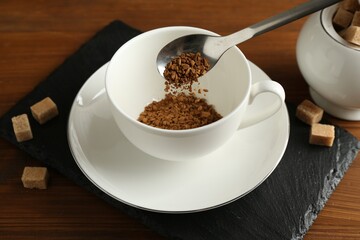 Putting granulated instant coffee into cup on wooden table, closeup
