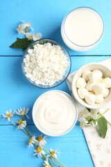 Different fresh dairy products and flowers on light blue wooden table, flat lay