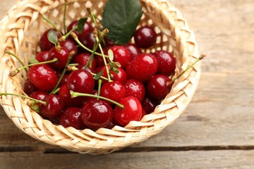 Fresh wet cherries and leaf in wicker basket on wooden table, closeup