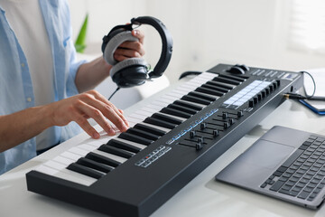 Man with headphones working with MIDI keyboard at white table indoors, closeup