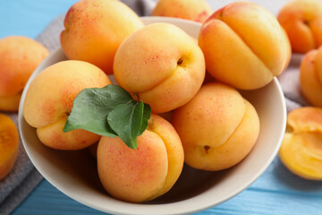 Fresh apricots with green leaves on light blue wooden table, closeup