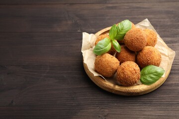 Delicious fried croquette balls with basil on wooden table. Space for text