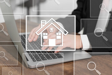 Real estate agent using laptop at table, closeup. House and magnifying glass icons on virtual screen