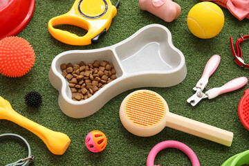 Food bowl in shape of bone and different pet accessories on green grass background