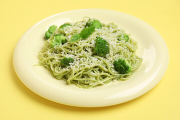 Plate of delicious spaghetti pasta with broccoli and basil leaves on yellow background, closeup