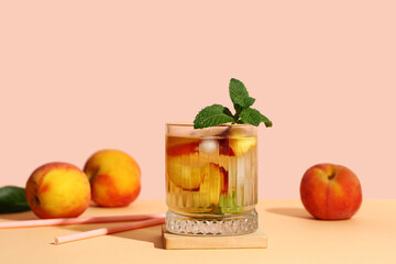 Glass of fresh peach lemonade with mint and fruits on orange table against beige background