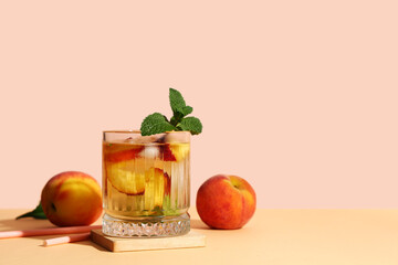 Glass of fresh peach lemonade with mint and fruits on orange table against beige background