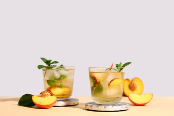 Glasses of fresh peach lemonade with mint on orange table against grey background