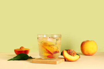 Glass of fresh peach lemonade with thyme on beige table against green background