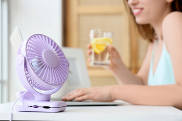 Small electric fan on table of young woman working with laptop