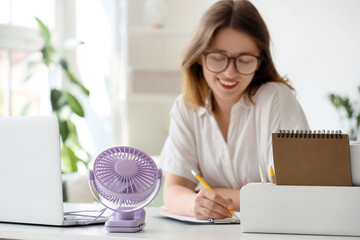 Small electric fan on table of young woman working in office