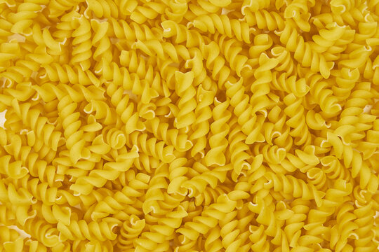 Full image of raw fusilli pasta, with a patterned background and copy space