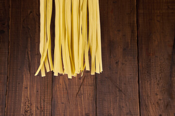 Fresh egg fettuccine noodles, drying in the foreground with a handmade wooden background with copy...