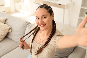 Young woman with dreadlocks taking selfie on sofa at home