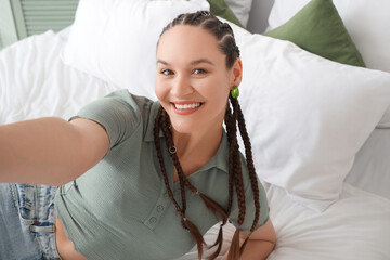 Young woman with dreadlocks taking selfie in bedroom