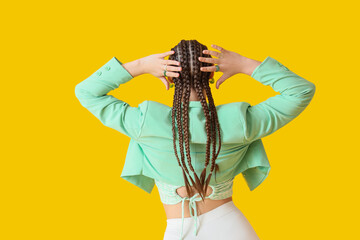 Stylish young woman with dreadlocks on yellow background, back view