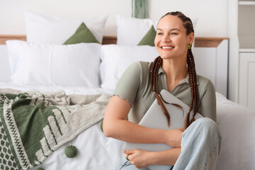 Young woman with dreadlocks and laptop sitting in bedroom
