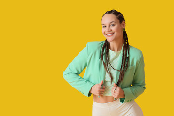 Stylish young woman with dreadlocks on yellow background