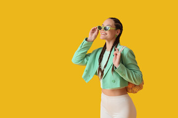 Stylish young woman with dreadlocks and string bag on yellow background