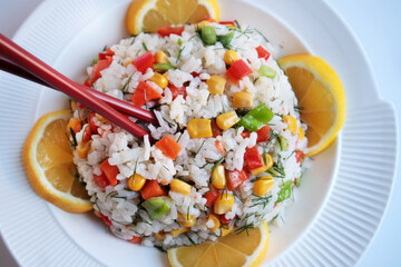 Rice salad or pilaf with colorful vegetables from Asian cuisine.,served with sliced lemon and chopsticks