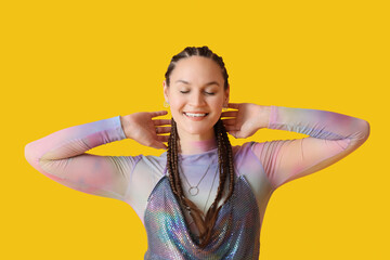 Fashionable young woman with dreadlocks smiling on yellow background