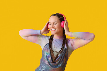 Fashionable young woman with dreadlocks and headphones on yellow background